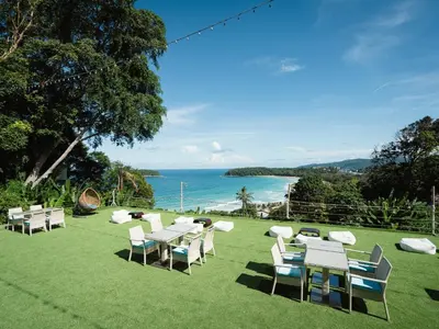 a group of tables and chairs on a lawn with the ocean at Andaman Cannacia Resort & Spa - SHA Extra Plus in Kata Beach