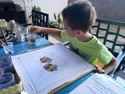 a young boy sitting at a table looking at a kite at Peach Blossom Resort & Pool Villa - SHA Plus in Kata Beach