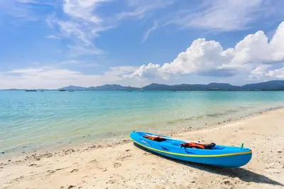 a blue kayak sitting on a beach next to the water at By The Sea in Panwa Beach