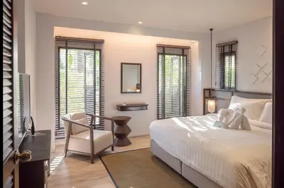 a bedroom with a bed and a chair and windows at The Pe La Resort, Phuket - SHA Extra Plus in Kamala Beach