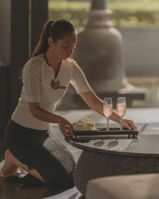 a woman sitting at a table with a tray with wine glasses at Twinpalms Surin Beach Phuket in Surin Beach