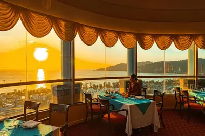 a woman sitting at a table in a restaurant looking out at the sunset at The Royal Paradise Hotel & Spa in Patong Beach