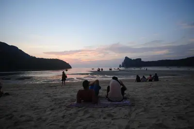 a group of people sitting on the beach watching the sunset at Phi Phi Twin Palms Bungalow in Phi Phi Don