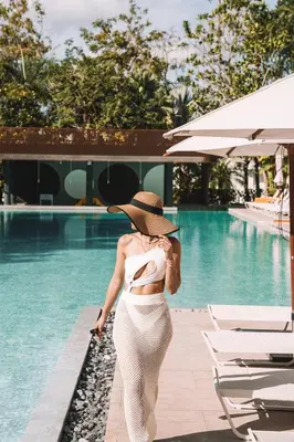 a woman in a hat walking by a swimming pool at Centara Karon Resort Phuket in Karon Beach