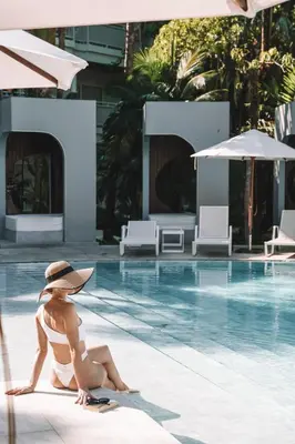 a woman in a hat sitting next to a swimming pool at Centara Karon Resort Phuket in Karon Beach