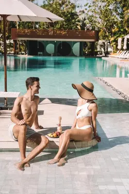 a man and a woman sitting next to a swimming pool at Centara Karon Resort Phuket in Karon Beach