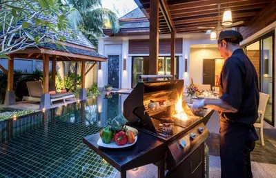 a man cooking food on a grill in a backyard at The Bell Pool Villa Resort Phuket in Kamala Beach