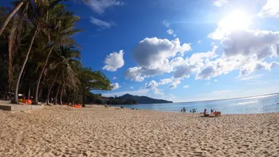 a beach with palm trees on a sunny day at Holiday Inn Resort Phuket Surin Beach by IHG in Surin Beach