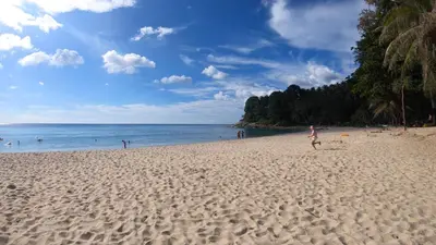 a person standing on a sandy beach near the ocean at Holiday Inn Resort Phuket Surin Beach by IHG in Surin Beach