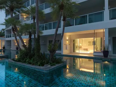a swimming pool with palm trees in front of a building at Chanalai Romantica Resort - Adults Only, Kata Beach in Kata Beach