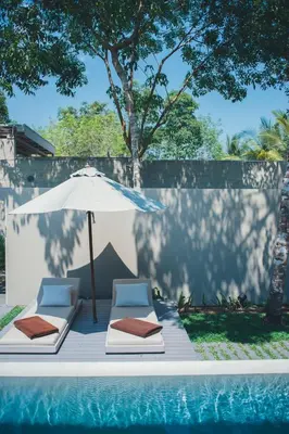 two lounge chairs and an umbrella next to a swimming pool at SALA Phuket Mai Khao Beach Resort in Mai Khao Beach