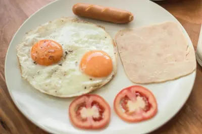 a plate with an egg and a sausage and tomatoes at Whalecome Aonang Resort-SHA Extra Plus in Ao Nang Beach