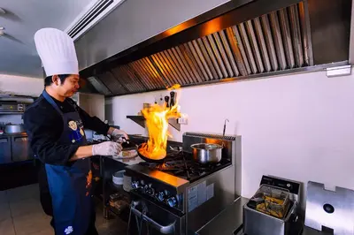 a man in a kitchen preparing food on a stove at Hotel Clover Patong Phuket - SHA Plus in Patong Beach