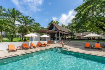 a woman walks by a swimming pool with orange chairs and umbrellas at Tinidee Golf Resort Phuket in Kathu