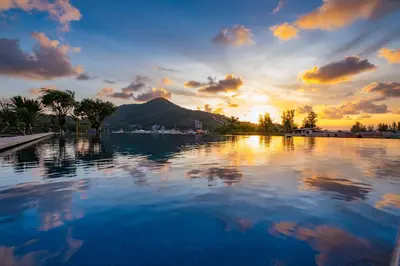 a pool of water with a sunset in the background at Kamala Resotel, SHA Extra Plus in Kamala Beach