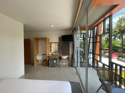 a bedroom with a bed and a desk and a balcony at Dwell Phuket Airport Hotel at Naiyang in Nai Yang Beach