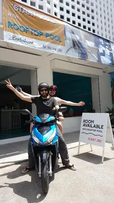two men sitting on a motor scooter in front of a building at Borbaboom Phuket Poshtel & Hostel in Phuket Town
