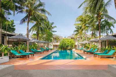 a pool with chairs and umbrellas and palm trees at Signature Phuket Resort in Chalong