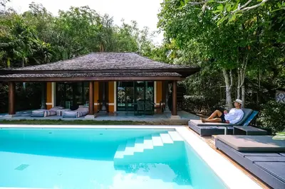 a man sitting on a chair next to a swimming pool at Bungalow VILLA Cha Cha in Ko Yao Noi