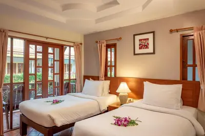 two beds in a hotel room with windows at Bangtao Village Resort - SHA in Bang Tao Beach