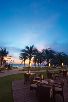 a patio with tables and chairs and palm trees at The Racha in Ko Racha Yai