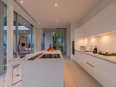 an open kitchen with white counters and glass walls at Villa Abiente in Thalang