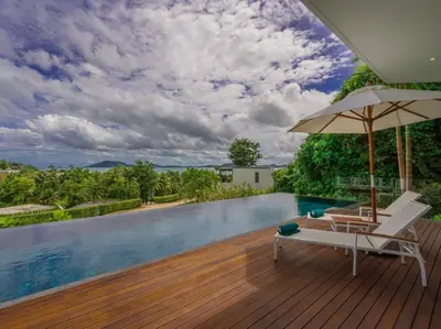 a pool with a chair and an umbrella on a wooden deck at Villa Abiente in Thalang