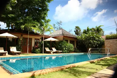 a swimming pool with chairs and umbrellas next to a house at Pai Tan Villas - SHA Extra Plus in Bang Tao Beach
