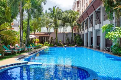 a swimming pool in front of a building with palm trees at Thanthip Beach Resort Patong in Patong Beach