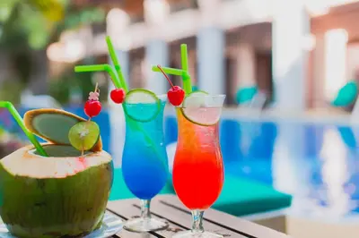 three cocktails sitting on a table next to a coconut at Thanthip Beach Resort Patong in Patong Beach