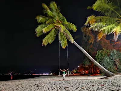 a person on a swing hanging from a palm tree on a beach at Seven Seas Hotel Patong Beach in Patong Beach
