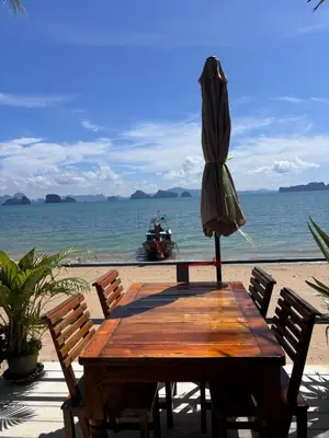 a wooden table with an umbrella next to the ocean at Mookdaman Bungalow in Ko Yao Noi