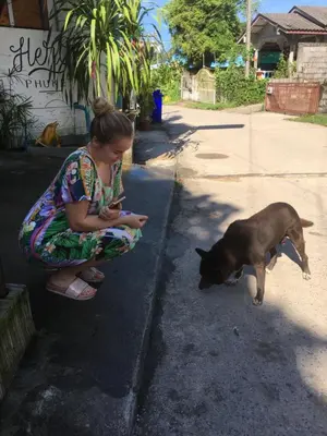 a woman sitting on the sidewalk next to a dog at Hero Phuket in Nai Yang Beach