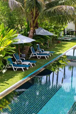 a pool with chairs and umbrellas next to a palm tree at Tea Tree Boutique Resort in Rawai Beach