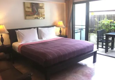 a bedroom with a bed with a purple blanket and a balcony at Kamala Beachfront Apartment in Kamala Beach