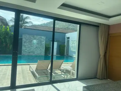 a room with glass doors and chairs next to a swimming pool at Skypool Villa by G Estate Phuket in Nai Harn Beach