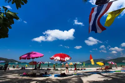 a group of people on a beach with umbrellas at Grand Orchid Inn Patong beach in Patong Beach