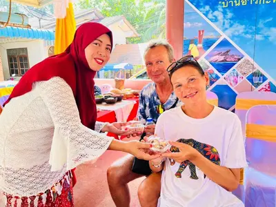 a woman holding a plate of food with two people at Banhalawee in Ko Yao Yai