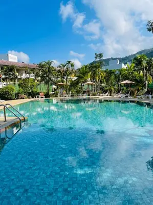 a large swimming pool at a resort with palm trees at Phuket Golden Sand Inn - SHA Extra Plus in Karon Beach