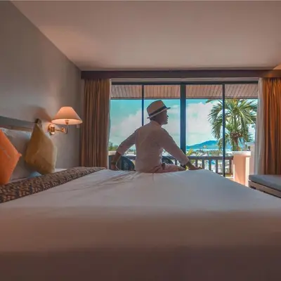 a man sitting on top of a large bed in a hotel room at C & N Resort and Spa - SHA Extra Plus in Patong Beach