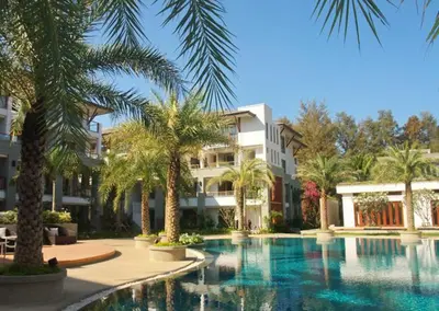 a swimming pool with palm trees in front of a building at Nai Thon Beachfront Apartments in Nai Thon Beach