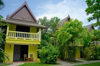 a yellow house with a balcony and trees at Chez Charly Bungalow in Nai Yang Beach