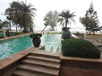 a swimming pool with stairs and palm trees and the ocean at Karon Sea View Beach Apartment in Karon Beach
