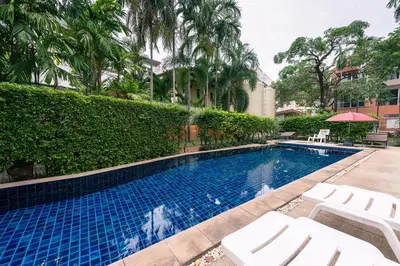 a swimming pool with white lounge chairs next to a hedge at Jinta Andaman in Kata Beach