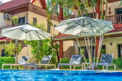 two umbrellas and chairs next to a swimming pool at Sai Rougn Residence - SHA Extra Plus in Patong Beach
