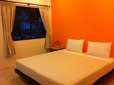 a bedroom with a bed with an orange wall and a window at Hacienda Phuket, Patong in Patong Beach