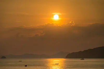 a sunset over the ocean with boats in the water at Sanim Hostel in Ao Nang Beach