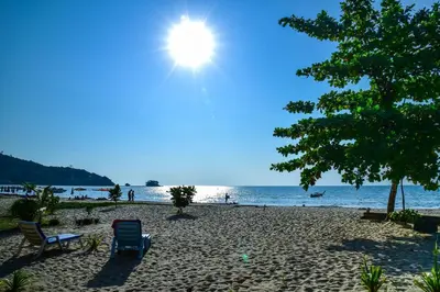 a beach with chairs and the sun in the sky at Dang Sea Beach Resort - SHA in Nai Yang Beach