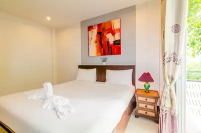 a bedroom with a white bed and a window at Baan Yuyen Karon Guesthouse in Karon Beach