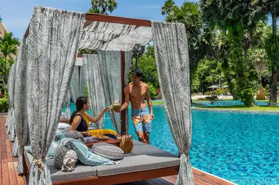 a man and a woman sitting on a bed next to a pool at Naithonburi Beach Resort - SHA Extra Plus in Nai Thon Beach